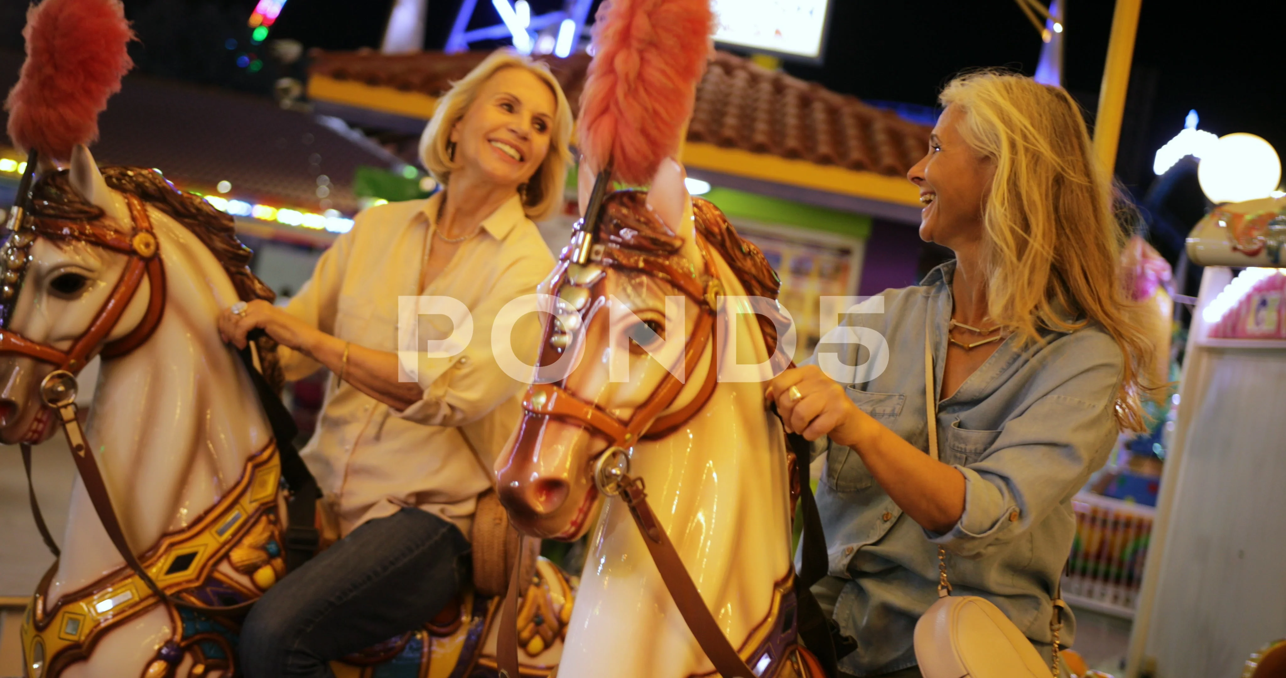 Fashionable mature women having fun on amusement park merry-go-round ride