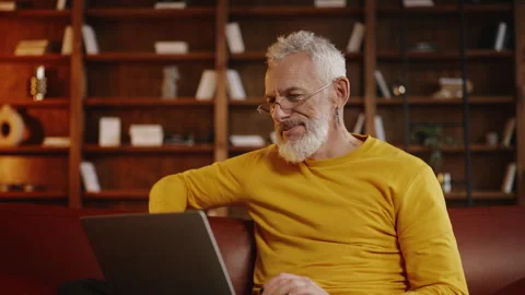 Fashionable middle-aged man using a laptop on a sofa to book vacation tickets Stock Footage 340902981