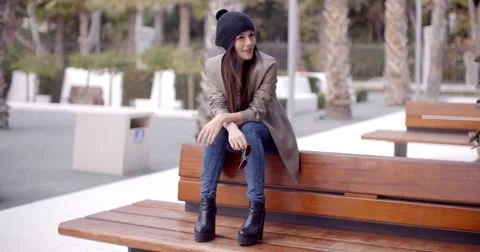Fashionable young woman sitting waiting on a bench Stock Footage