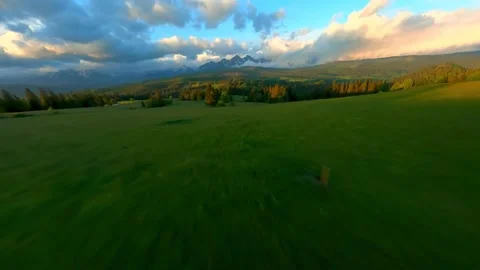 Fast aerial flight over a green meadow toward rocky peaks at sunset Stock-Footage 341329262