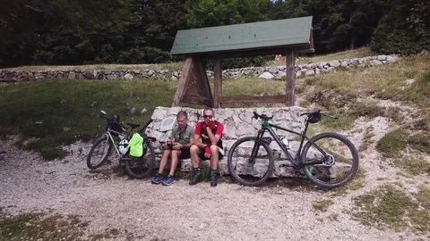 Fast aerial pull back, cyclists resting near a mountain path, in a sunny morning Stock Footage 113040550