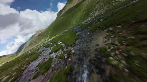 Fast aerial tracking shot over mountain stream and grassy slopes Video stock 345088602