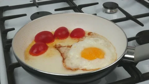 Fast breakfast - eggs, tomatoes and sausages are fried in a pan with a white Stock Footage 134309573