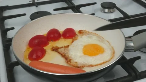 Fast breakfast - eggs, tomatoes and sausages are fried in a pan with a white Stock Footage 134309578