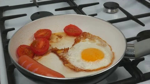 Fast breakfast - eggs, tomatoes and sausages are fried in a pan with a white Stock Footage