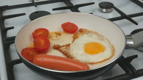 Fast breakfast - eggs, tomatoes and sausages are fried in a pan with a white Stock Footage 134309605
