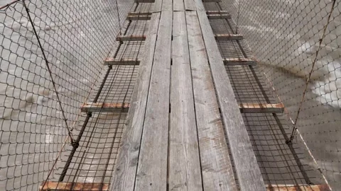 Fast brown river flowing under the rope bridge with wooden planks Stock-Footage 275614541