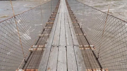 Fast brown river flowing under the rope bridge with wooden planks Stockbeeldmateriaal 276190050