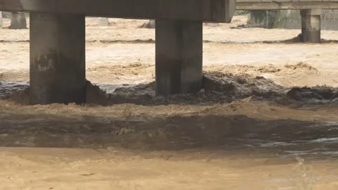 Fast floodwater surges between concrete bridge - Raging Stream and Rain Swollen Stock Footage 339744254