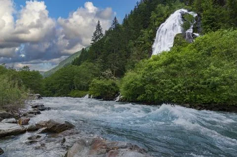 Fast flow of alpine river and beautiful waterfall in the mountain valley 스톡 사진