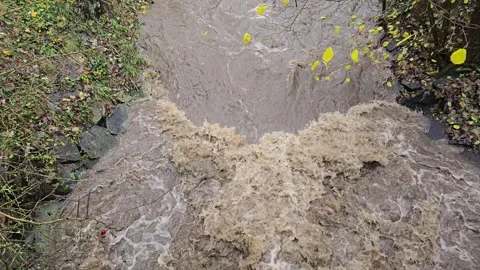 Fast flowing flooded river with waterfall after storm rain in slow motion Video stock 320936058