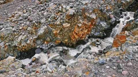Fast-flowing glacial stream through rugged, colorful rock formations on the Glac Stock Footage 332141875
