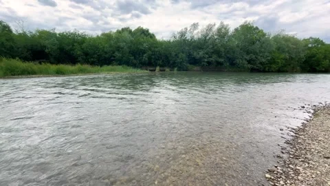 A fast flowing river with ripples runs under an overcast cloudy sky.  Video stock 339092197