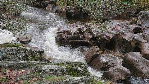 A fast flowing river winds its way down stream through large rocks. 4K tripod Stock Footage 222742818