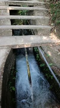 Fast flowing water stream flowing under concrete steps in rural area Stock Photos