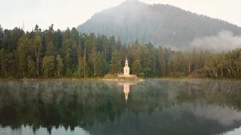 Fast flying drone above throw up church, autumn forest on island inside lake Stock Footage 107901907