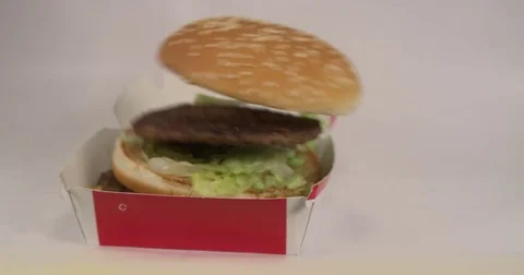 Fast food beef burger falling in slow motion. Filmed in box packaging and text Stock Footage 72575819