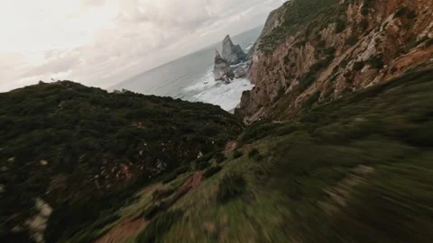 Fast FPV dive from rocky green cliff toward Ursa Beach coastline during sunset Stock Footage 336201947