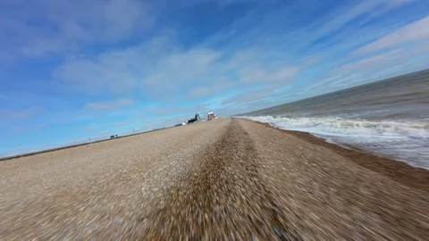 Fast FPV drone low flight over the pebble beach and crashing waves at Aldeburgh Stock Footage 342080744