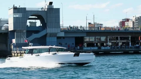 Fast motor boat in slow motion and passing in front of The Galata Bridge Stock Footage 346297947