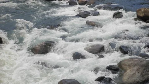 Fast mountain river rapids splashing between dark boulders in slow motion 動画素材 348705812