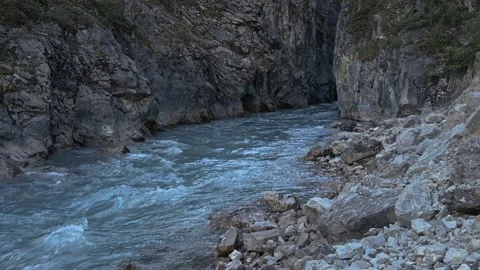 A fast-moving blue-grey colored river emerges from a large rock crevasse Stock Footage 139467079