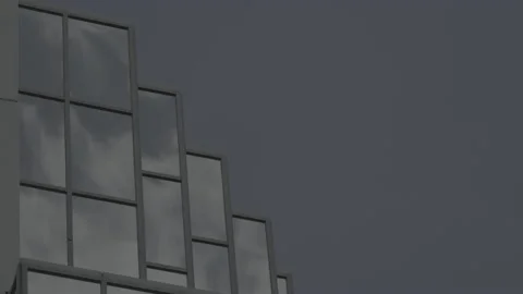 Fast moving clouds reflected in office windows against blue sky Stock Footage 135196199