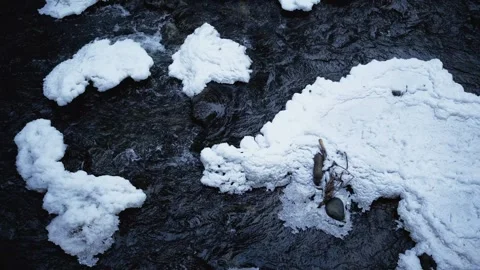 A fast-moving river flows through a winter landscape, with patches of snow resti Stock Footage 303486254