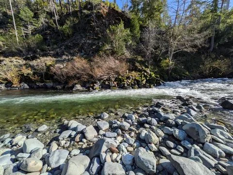 Fast-moving river rapids crash over rocks beside mossy hills and thick greenery Stockfoto's