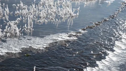 Fast moving stream of narrow river runs along frozen banks on sunny day Stock Footage 224535938