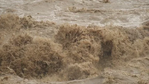 Fast muddy floodwaters rush through river channel with violent flow - Flood Risk Vidéo 339750570