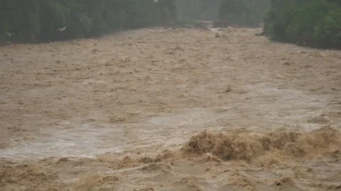 Fast muddy floodwaters rush through river channel with violent flow - High Water Stock Footage 339750587