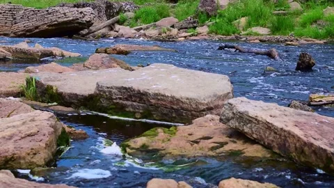 A fast river with blue water flows between large stones, grass grows on the bank Stock Footage 156623469