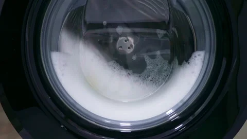 Fast spinning washing machine drum rotating clothes with water during laundry Stock Footage 266006973
