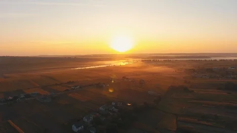 Fast-tracking drone footage at sunset time above fields with houses, which slows Stock Footage 124028076