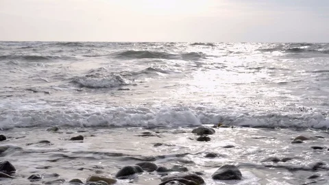 Fast waves at beach with rounded stones and the sun reflects at the surface Stock Footage 128986415