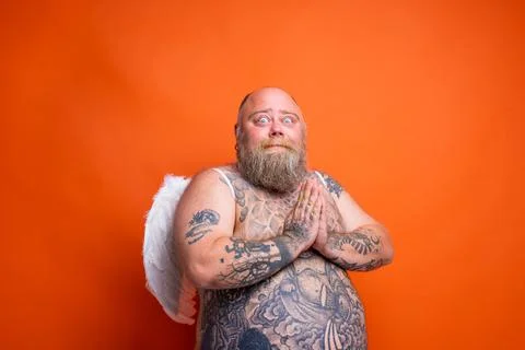 Fat afraid man with beard ,tattoos and wings acts like an angel Stock Photos