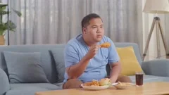 Greedy man watching TV while eating junk, Stock Video