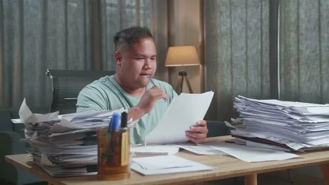 Fat Asian Man Thinking Then Taking Note While Working With Documents Stock Footage 196112759