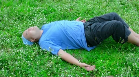 A fat bald head Thai man is lying on the green grass, relaxing and stretching Stock Footage 63214631