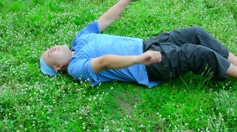 Fat bald head Thai man is lying on the soft green grass, relaxing and stretching Stock Footage 63214719