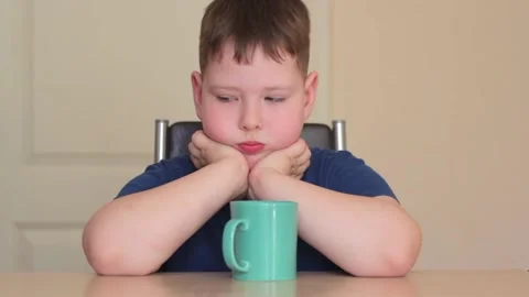 A fat child is sitting at a table with his chin in his hands. Video stock 169810295