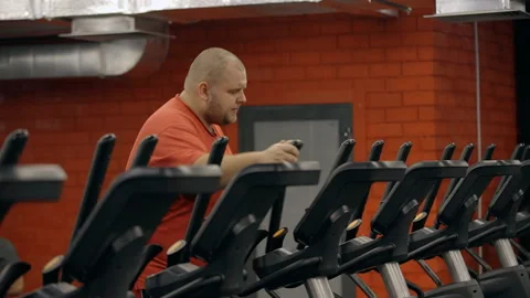 Fat exhausted man working out on elliptical trainer in gym to lose weight Stock Footage 119396115
