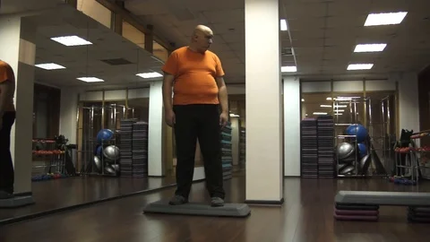 Fat funny man is standing on a step in a fitness room with a confused look 스톡 동영상 97092195