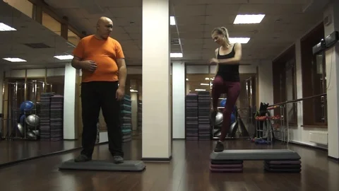 Fat funny man is standing on a step and looking at young sportswoman 스톡 동영상 97092228