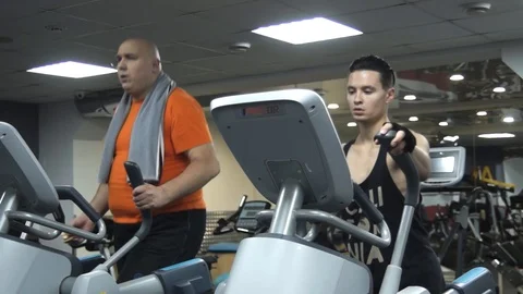 Fat funny man training on an ellipsoid holding hamburger 스톡 동영상 96555594