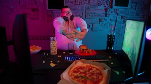 The Fat gamer plays at the computer and eats a burger and pizza. A Thick program 動画素材 220420705