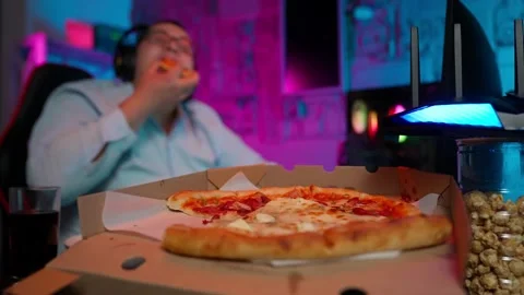 The Fat gamer plays at the computer and eats a burger and pizza. A Thick program 動画素材 220422924