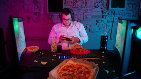 The Fat gamer plays at the computer and eats a burger and pizza. A Thick program Stock Footage 220423560