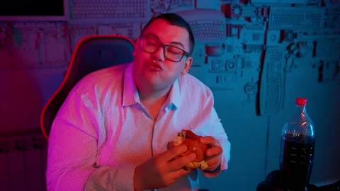 The Fat gamer plays at the computer and eats a burger and pizza. A Thick program 動画素材 220423992